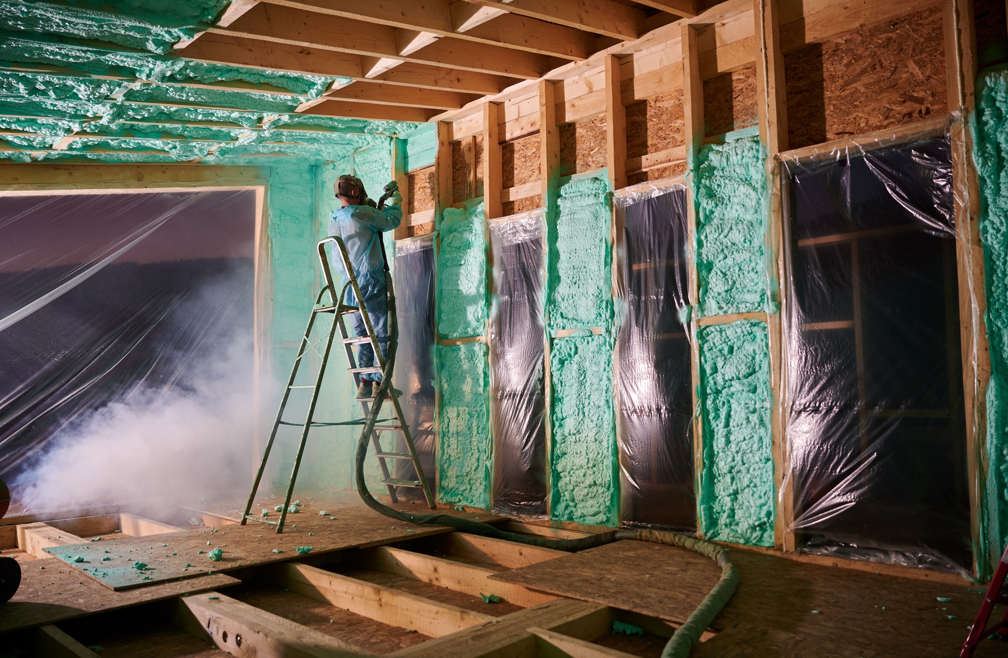 Worker spraying polyurethane foam for insulating wooden frame house.